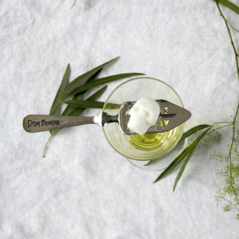 Absinthe glass, sugar cube skull on absinthe spoon, green leaves, white background, absinthe cocktail.