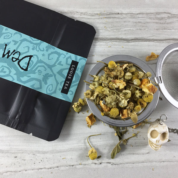 Close up of Herbal Tea spilling out of black bag on Marble tile, Tea in tea ball with skull bead, Dried Chamomile Mint &  Orange