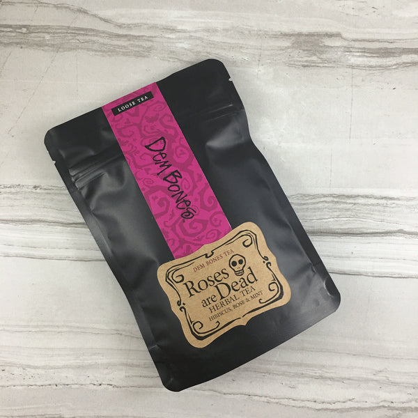 Black bag of tea on light tile, Pink and Kraft Labels, DemBones Tea, Roses are dead, Herbal Tea, Hibiscus rose & mint